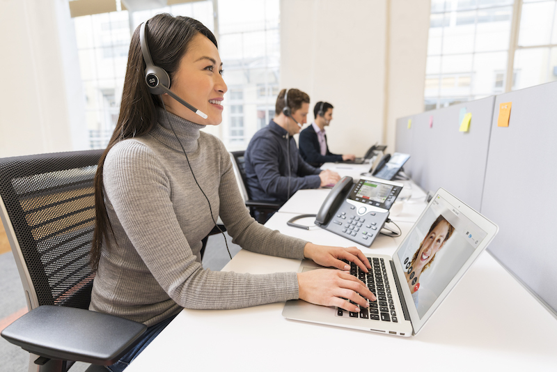 Eine Frau nutzt im Büro das Headset, den Laptop und das IP-Telefon zur Kommunikation