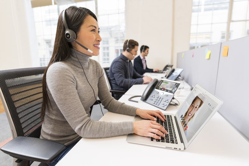 Eine Frau nutzt im B&uuml;ro das Headset, den Laptop und das IP-Telefon zur Kommunikation