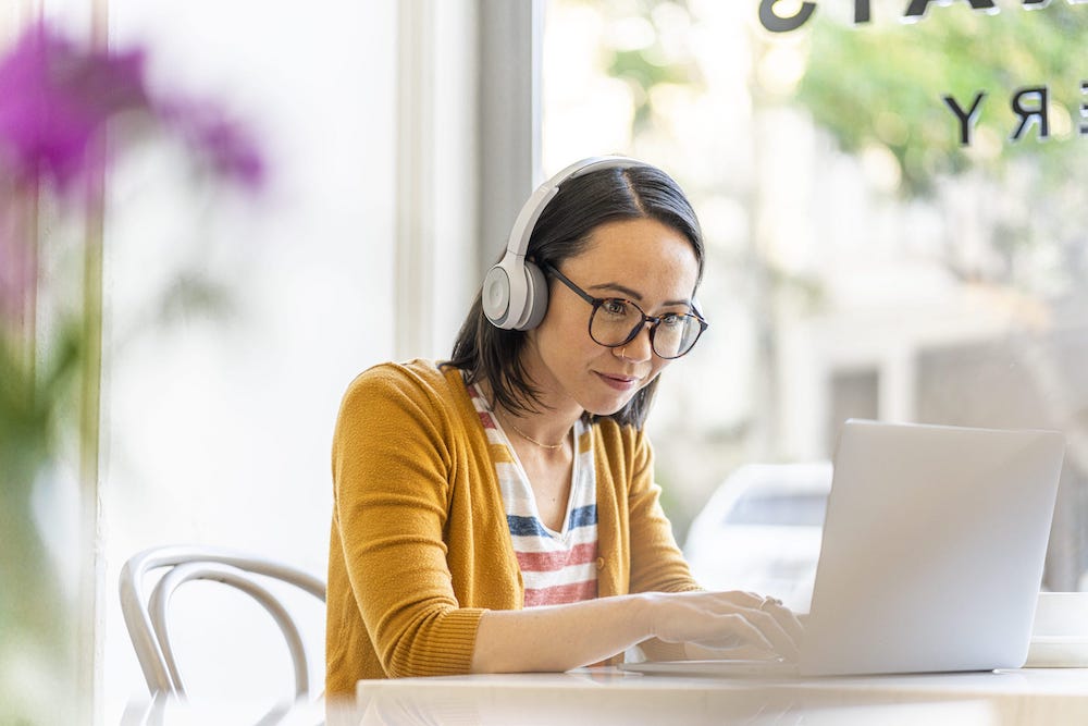 Eine Frau tr&auml;gt das Cisco 730 Headset in der Farbe Platinum bei der Arbeit aus dem Caf&eacute;