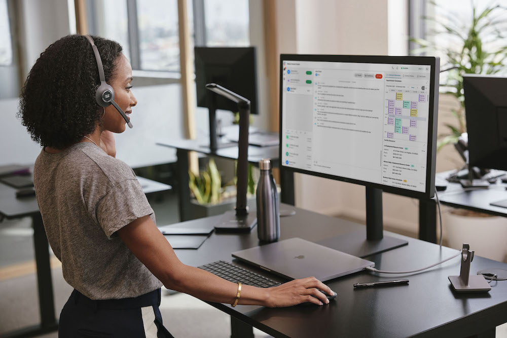 Eine Frau tr&auml;gt wichtige Daten &uuml;ber den Comuter in das Onlinesystem des Unternehmens ein, w&auml;hrend sie &uuml;ber das Headset telefoniert