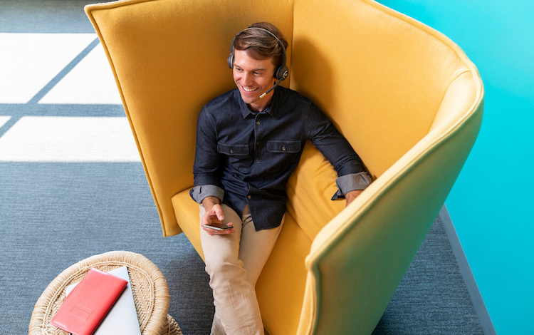 Ein Mann sitzt in einem modernen Sessel, w&auml;hrend er &uuml;ber sein Mobiltelefon und das Cisco Headset telefoniert