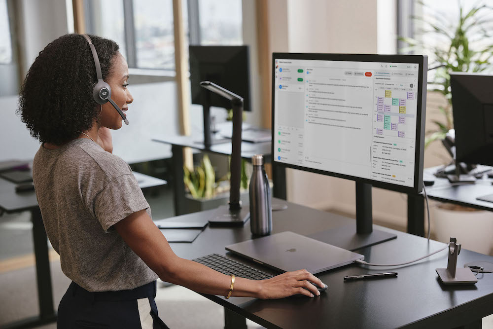 Eine Frau trägt wichtige Daten über den Comuter in das Onlinesystem des Unternehmens ein, während sie über das Headset telefoniert
