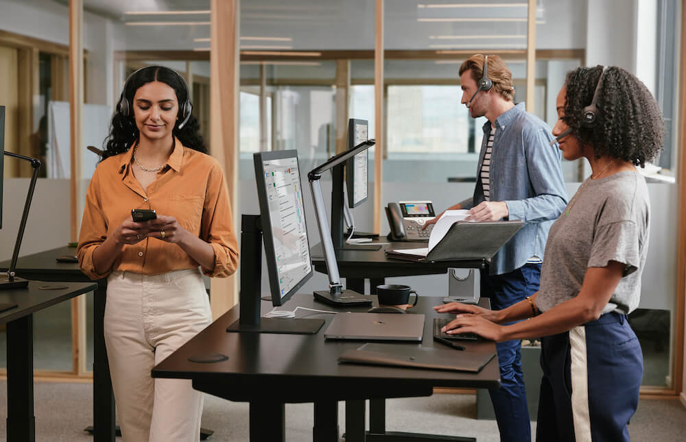Eine Frau läuft mit ihrem Cisco-Headset durch das Büro, während ihre Kollegen am Computer arbeiten und über ihre Headsets telefonieren