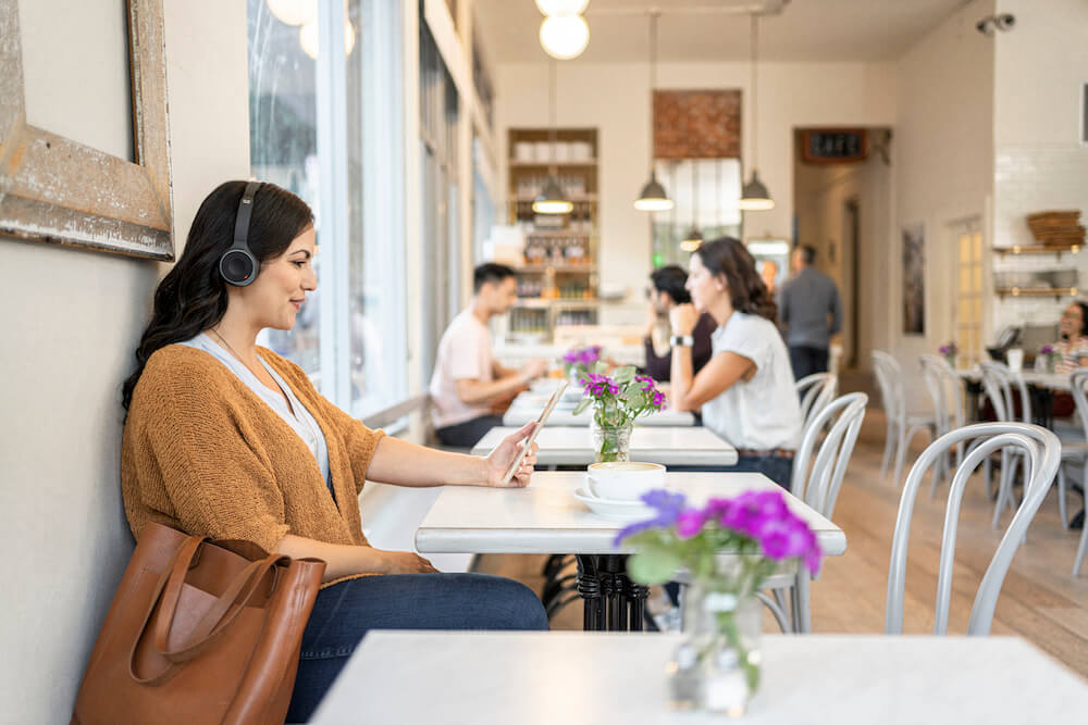 Eine Frau tr&auml;gt in einem Caf&eacute; das Cisco 730 Headset und liest