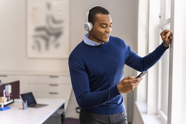 Ein Mann lehnt sich an das Fenster seines Homeoffice, w&auml;hrend er &uuml;ber das Cisco 730 Headset telefoniert