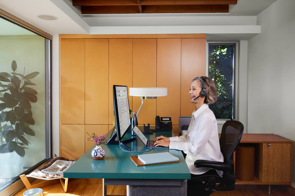 Eine Frau nutzt ihr Headset im Homeoffice für die Telefonie, während sie am Computer arbeitet