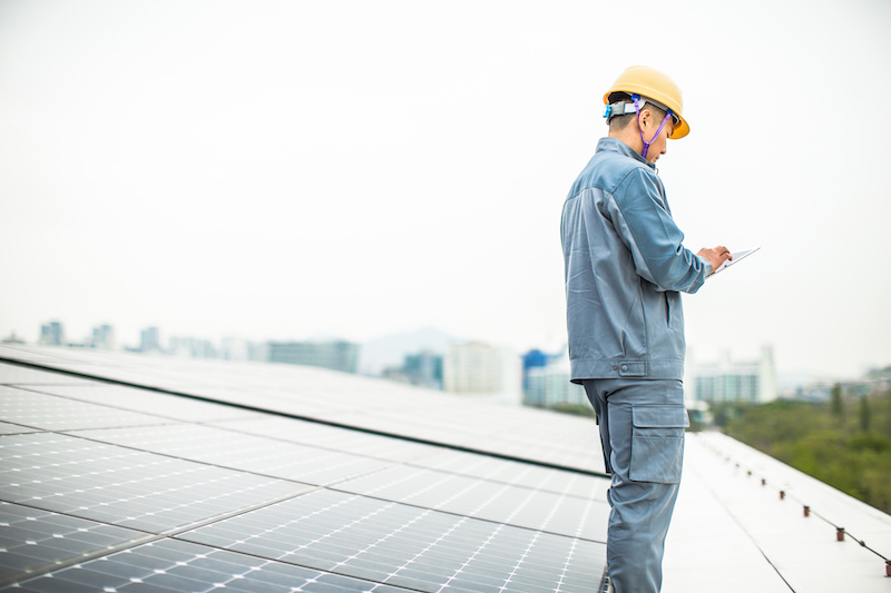 Ein mobiler Arbeiter mit Helm steht auf einer Solaranlage