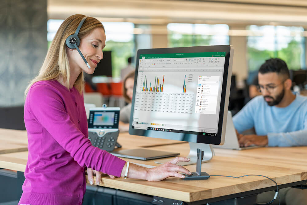 Eine Frau telefoniert im B&uuml;ro &uuml;ber das Headset und Cisco-Telefon, w&auml;hrend sie wichtige Daten auf dem Computer aufruft
