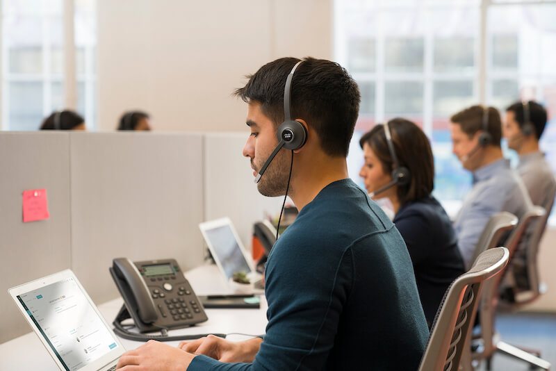EIn Mann telefoniert im Gro&szlig;raumb&uuml;ro &uuml;ber das Headset und das Cisco-Telefon, w&auml;hrend er etwas in den Laptop eintr&auml;gt