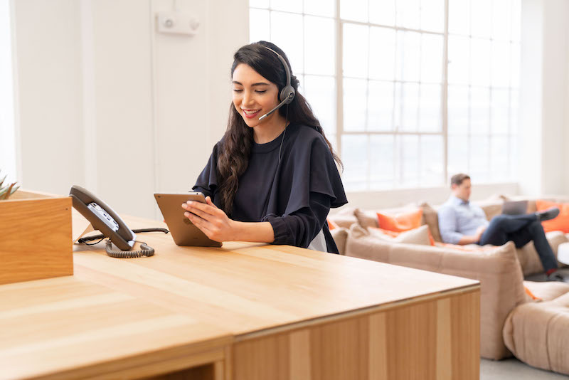 Eine Frau sitzt an einem Tisch und telefoniert über das Headset und ihr Cisco-Telefon, während sie mit dem iPad arbeitet