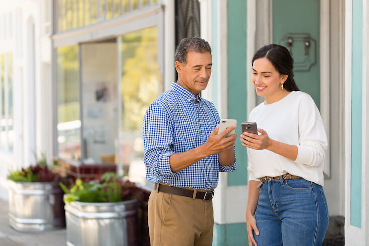 Ein Mann und eine Frau nutzen im Au&szlig;enbereich des Caf&eacute;s das G&auml;ste-Wifi per Handy