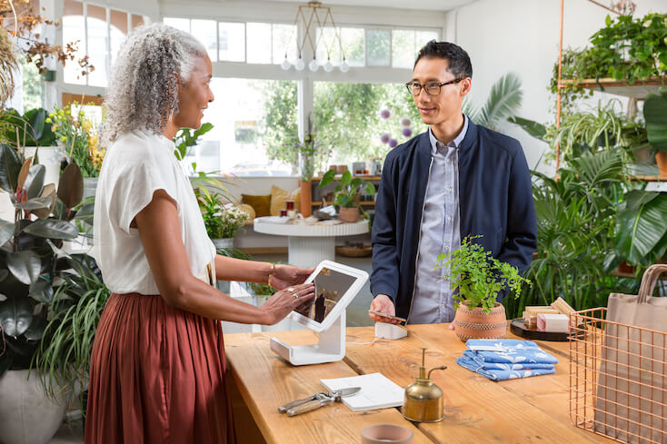 Ein Mann und eine Frau nutzen eine moderne Kasse f&uuml;r den Bezahlvorgang in einem Blumengesch&auml;ft